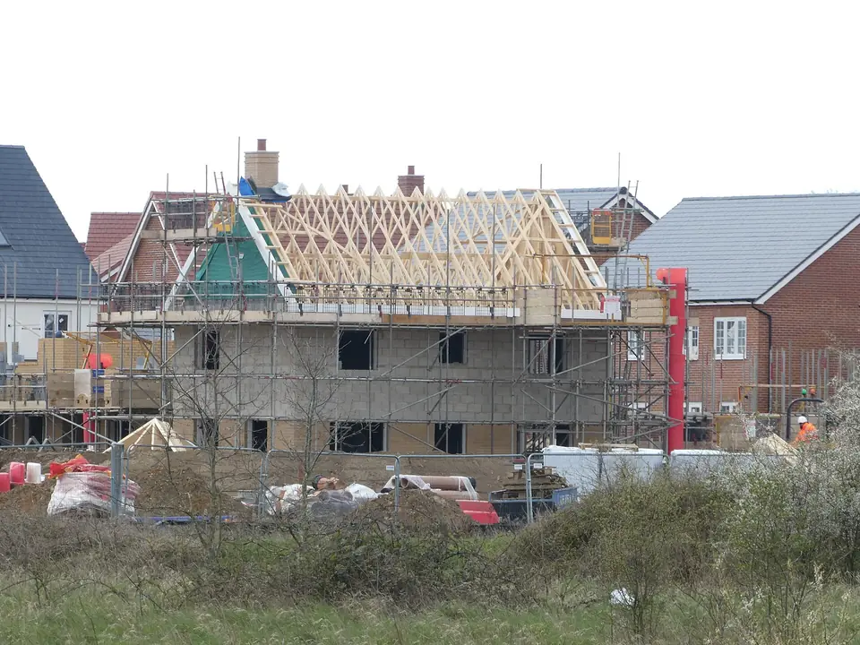 Maison neuve en construction à Wymondham, fermettes de charpente en bois posées sur les murs, entourée d'échafaudages et de matériaux.