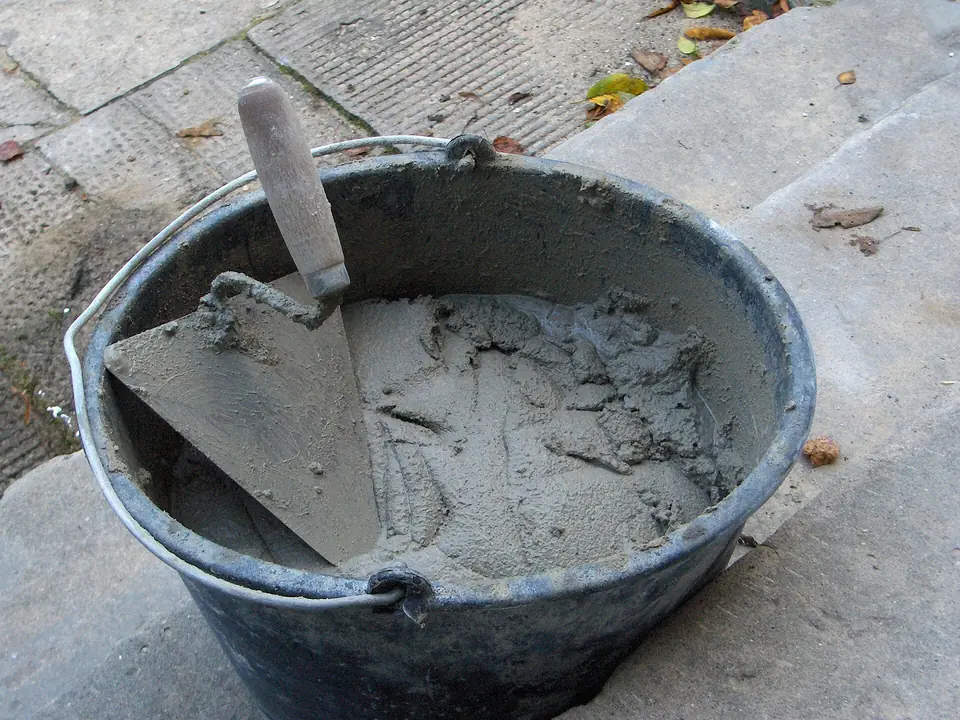 Truelle de maçon plantée dans un seau rempli de mortier frais, posé sur une dalle en béton.